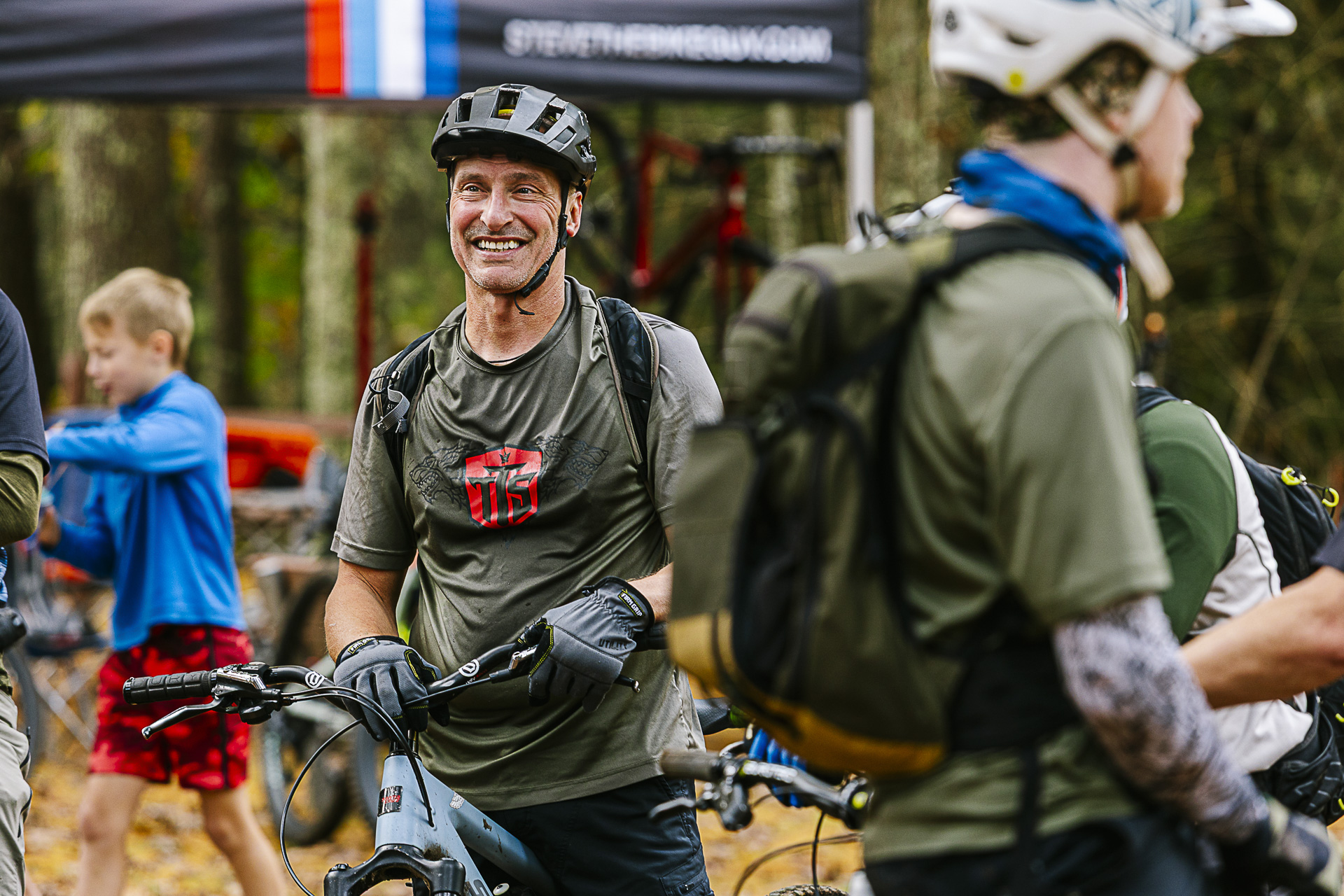A grinning rider waits in the busy staging area among riders and kids