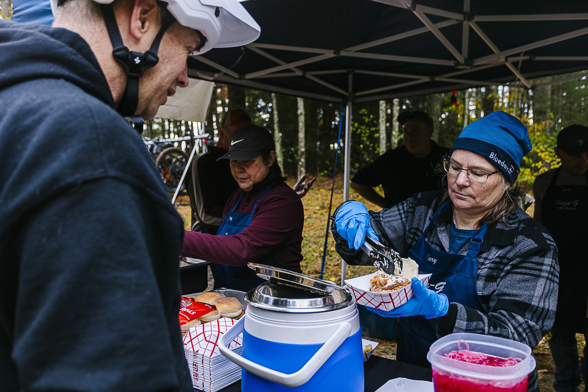 Volunteers in gloves serve barbecue from under a tent