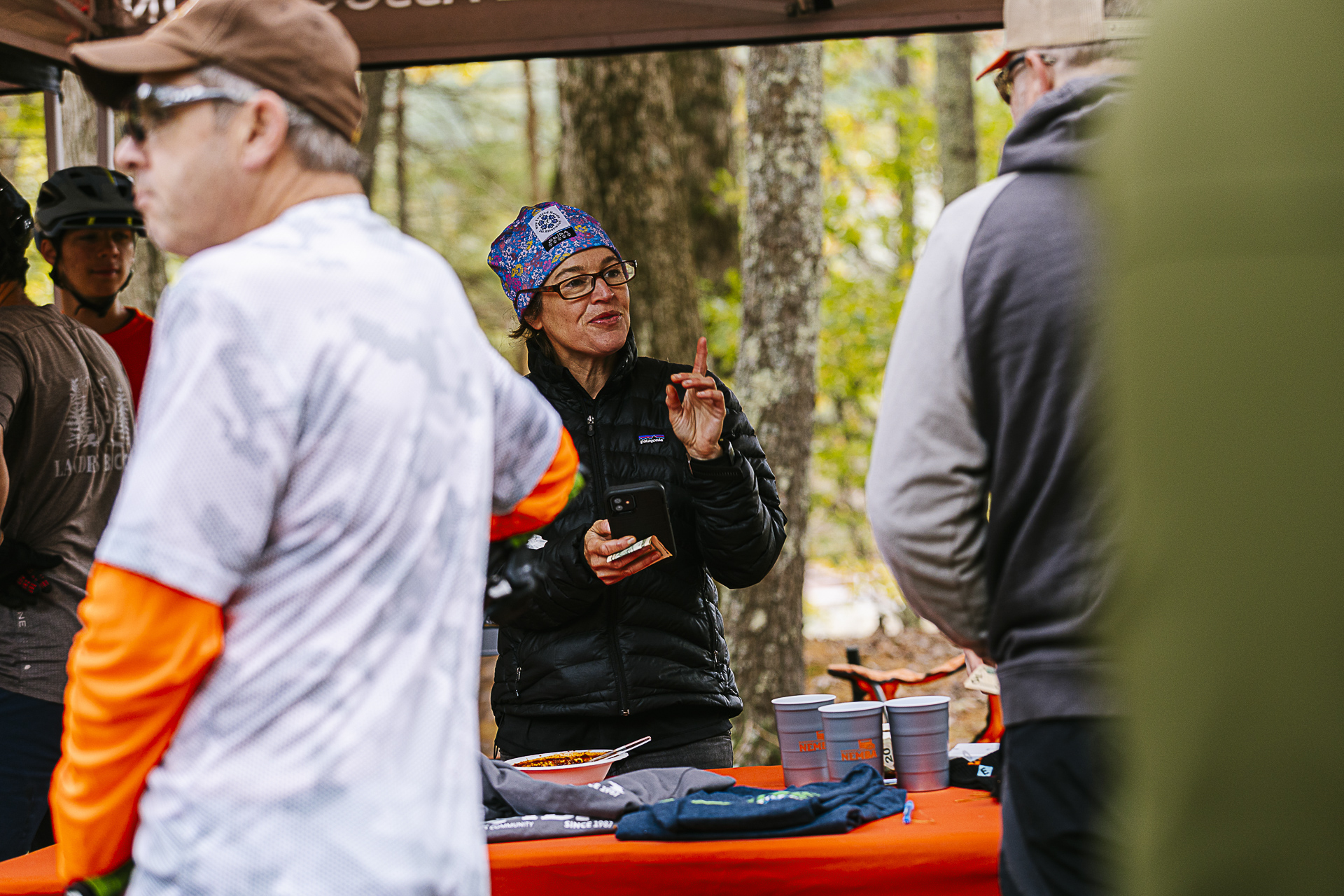 A woman in a patterned headband chats with riders across a tent table