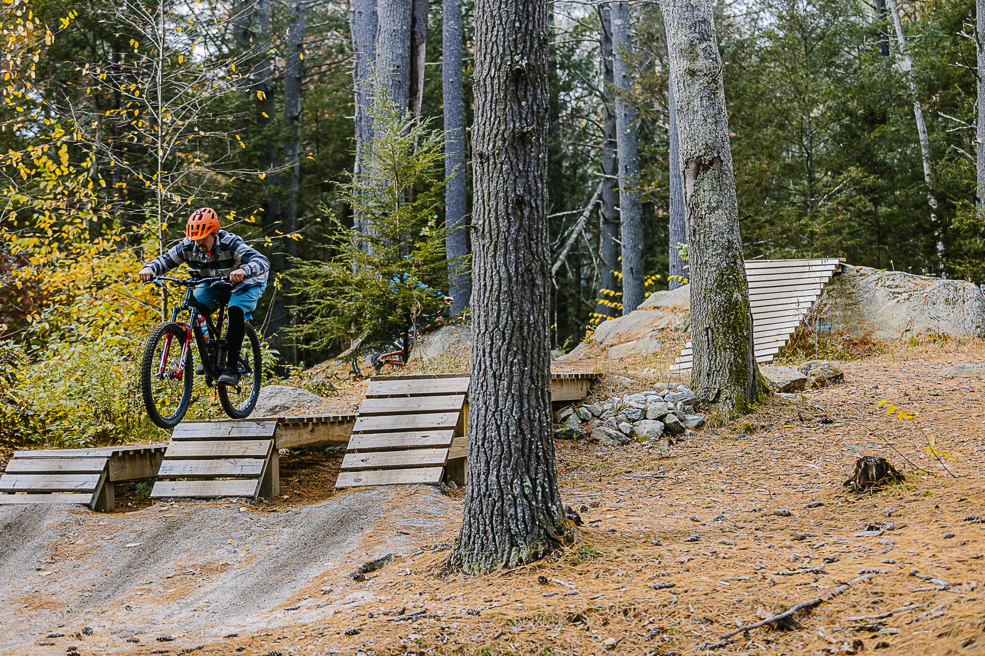 A rider in an orange helmet drops off a wooden feature in the skills park