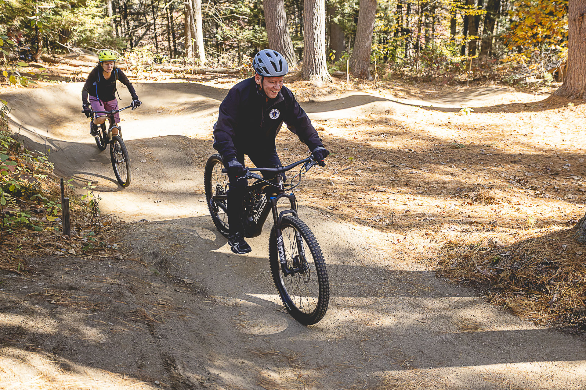 Two riders carve through banked dirt turns on a flow track