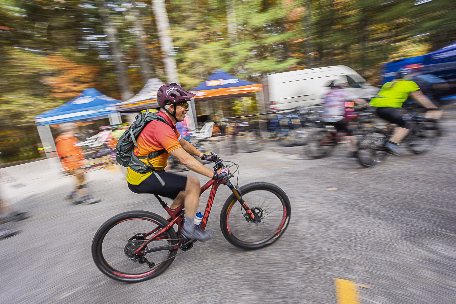 A rider in an orange jersey speeds past the vendor tents