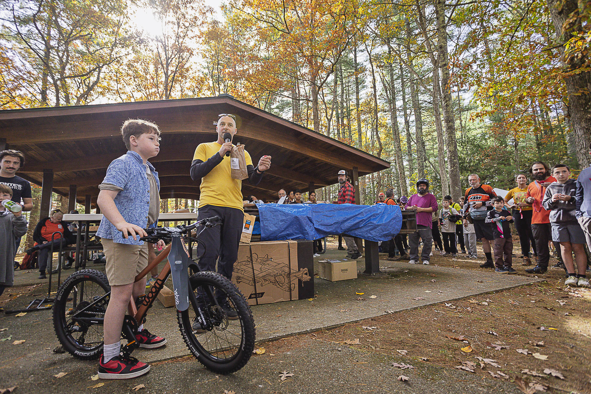 A young rider stands with a bike as an emcee with a microphone addresses the crowd at the pavilion