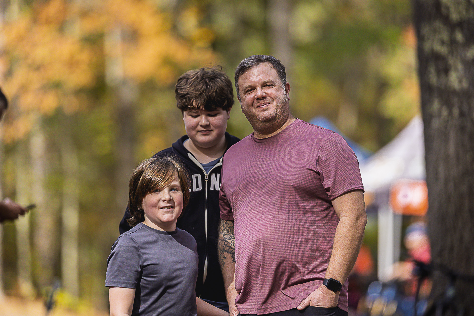 An adult and two boys pose together near the vendor tents