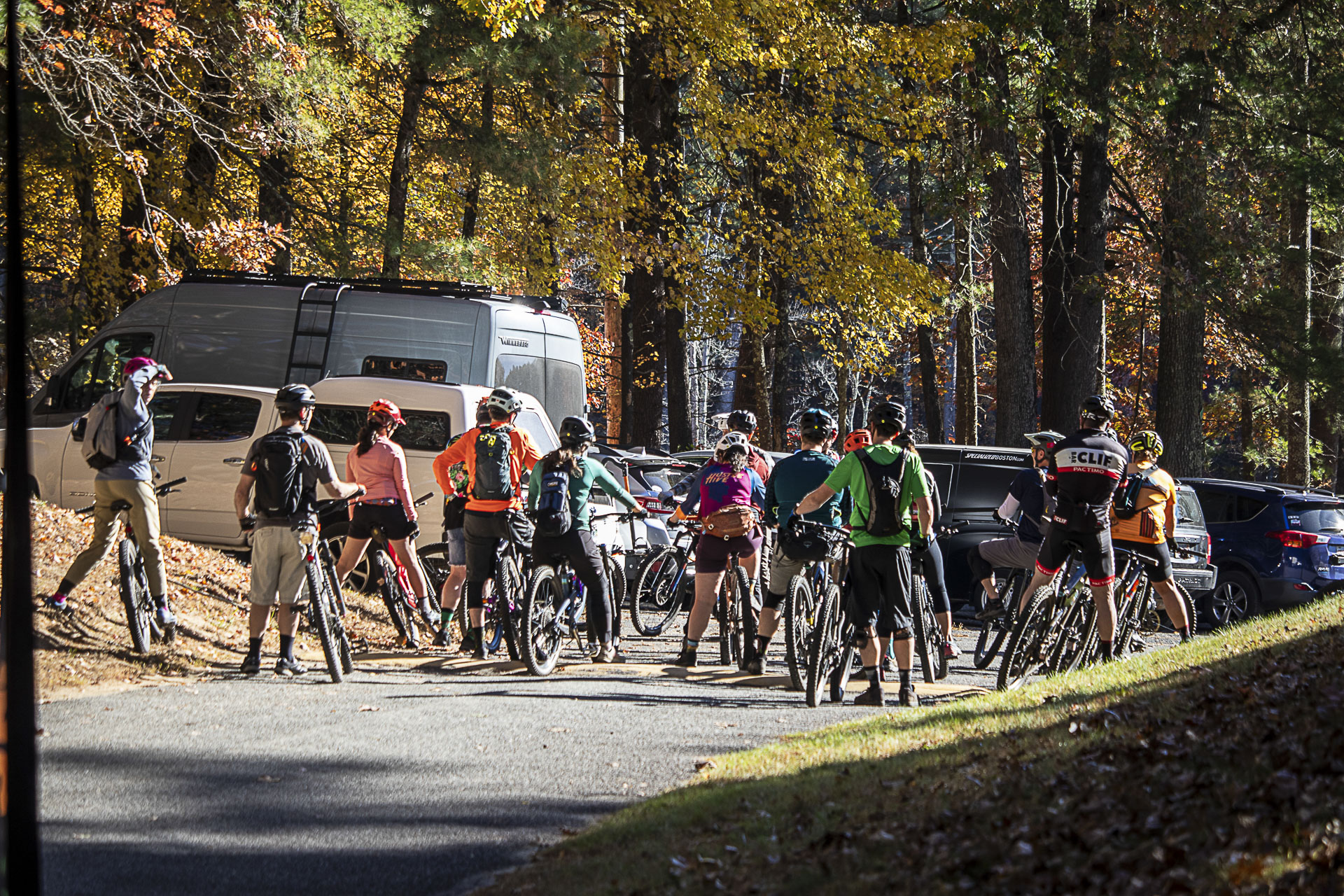 A large group of riders gathers in the parking area before heading out