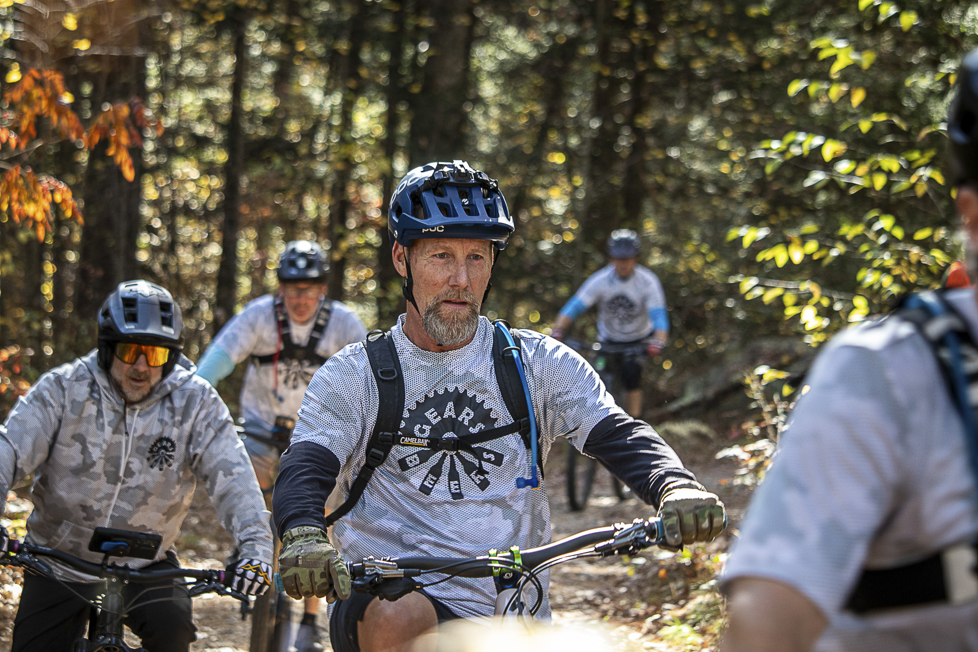 A pack of riders rolls down a sunlit wooded trail